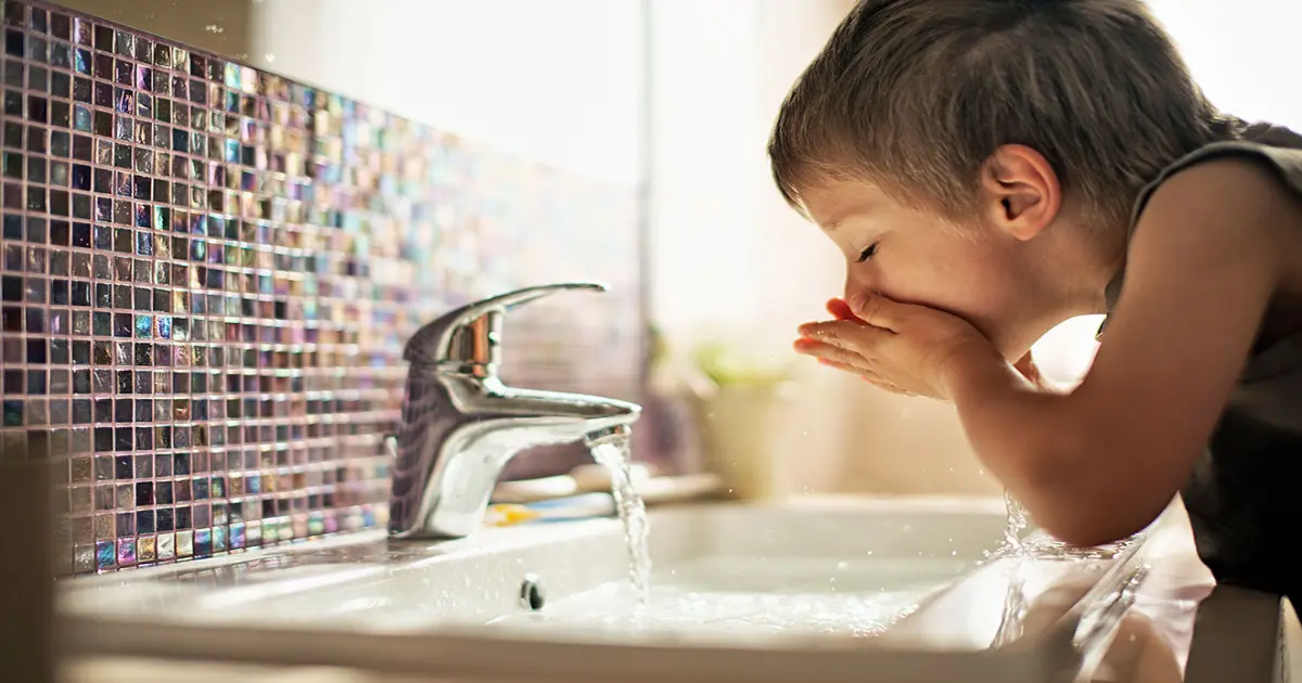 Junge im Badezimmer trink Wasser aus dem Hahn.