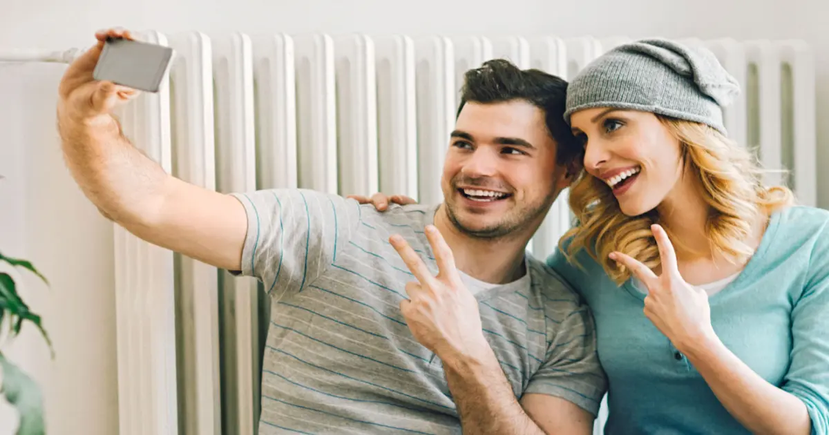 Paar sitzt vor der Heizung und fotografiert ein Selfie.