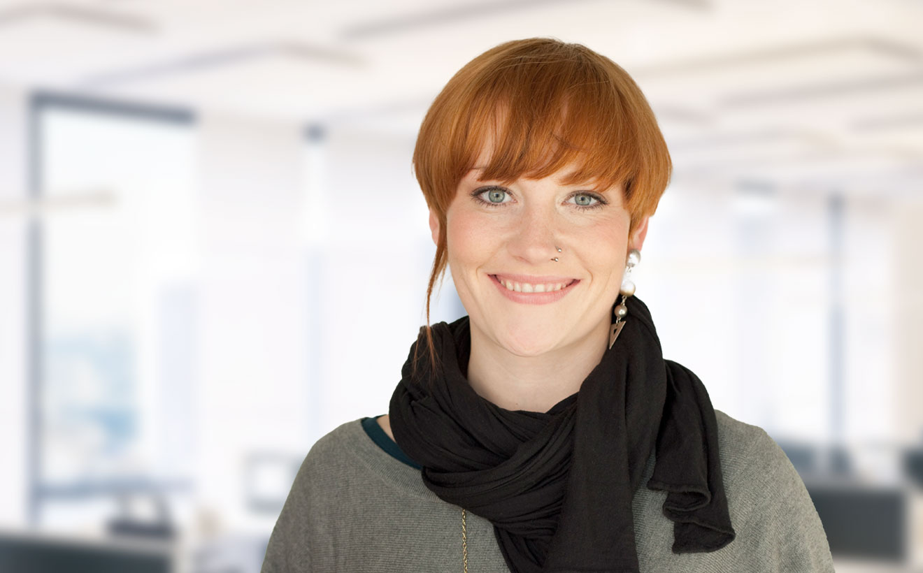 Lächelnde, junge Frau mit rötlichen Haaren, modisch gekleidet.