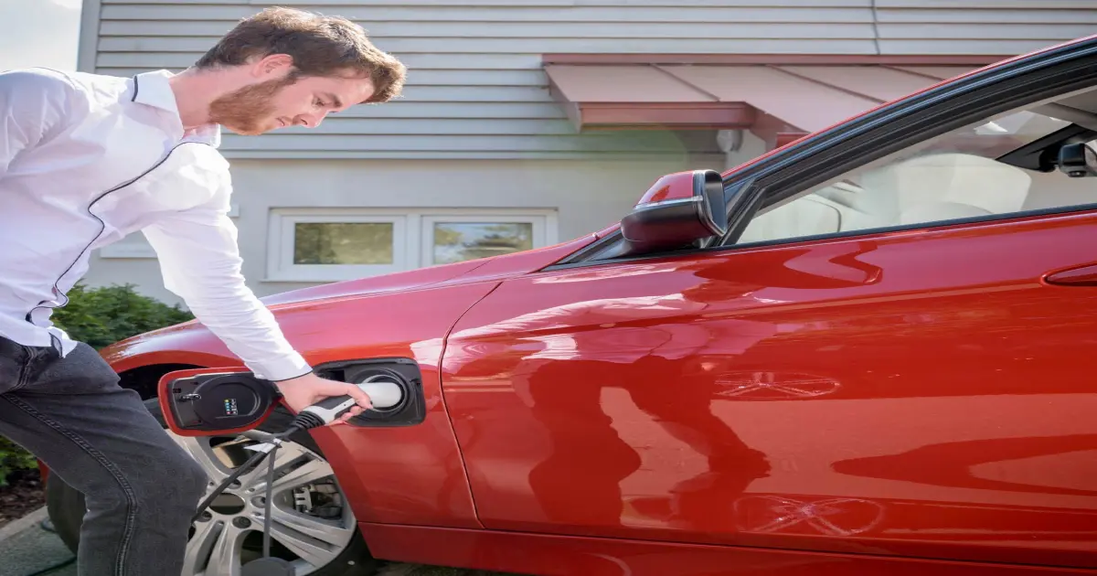 Junger Mann lädt sein Elektroauto zuhause.