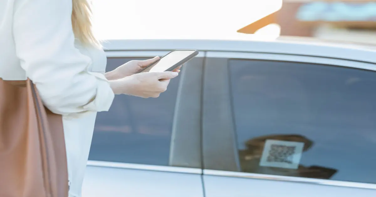 Frau mit Smartphone am KFZ