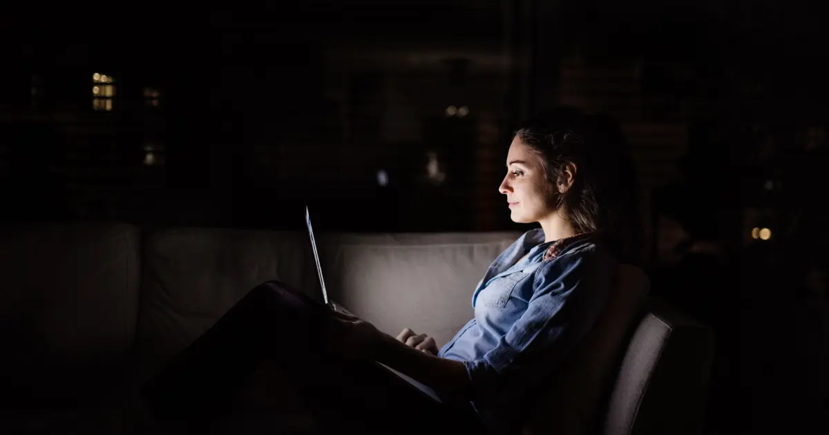 Frau sitzt im Dunkeln vor ihrem Laptop.