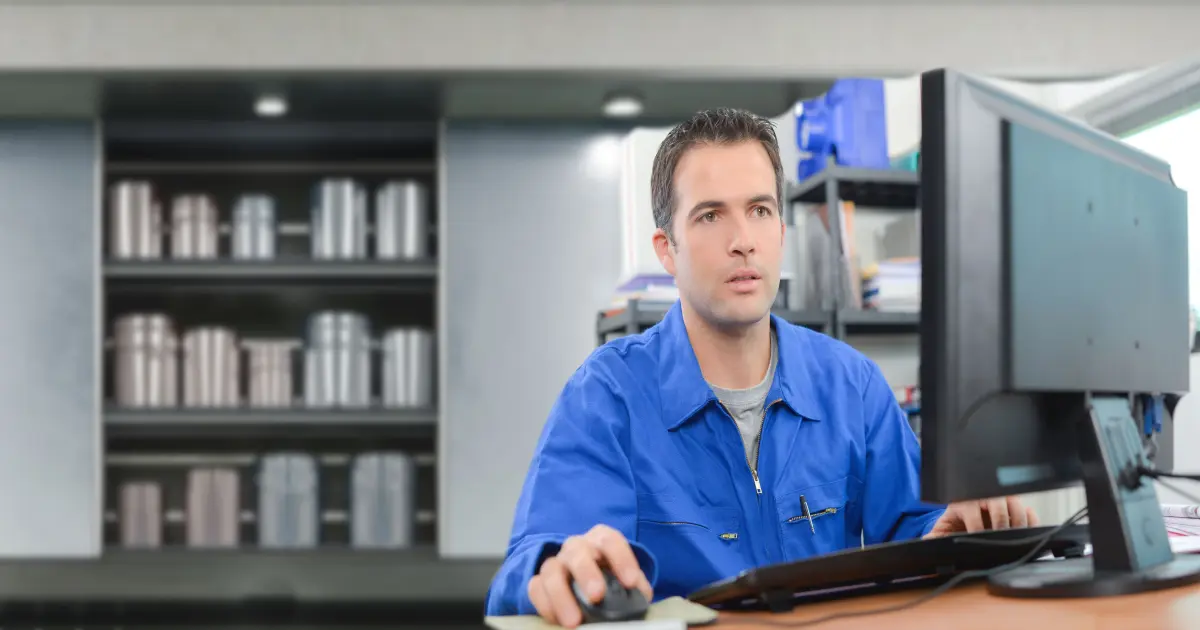 Ein Mensch im Blaumann sitzt vor einem Computerbildschirm