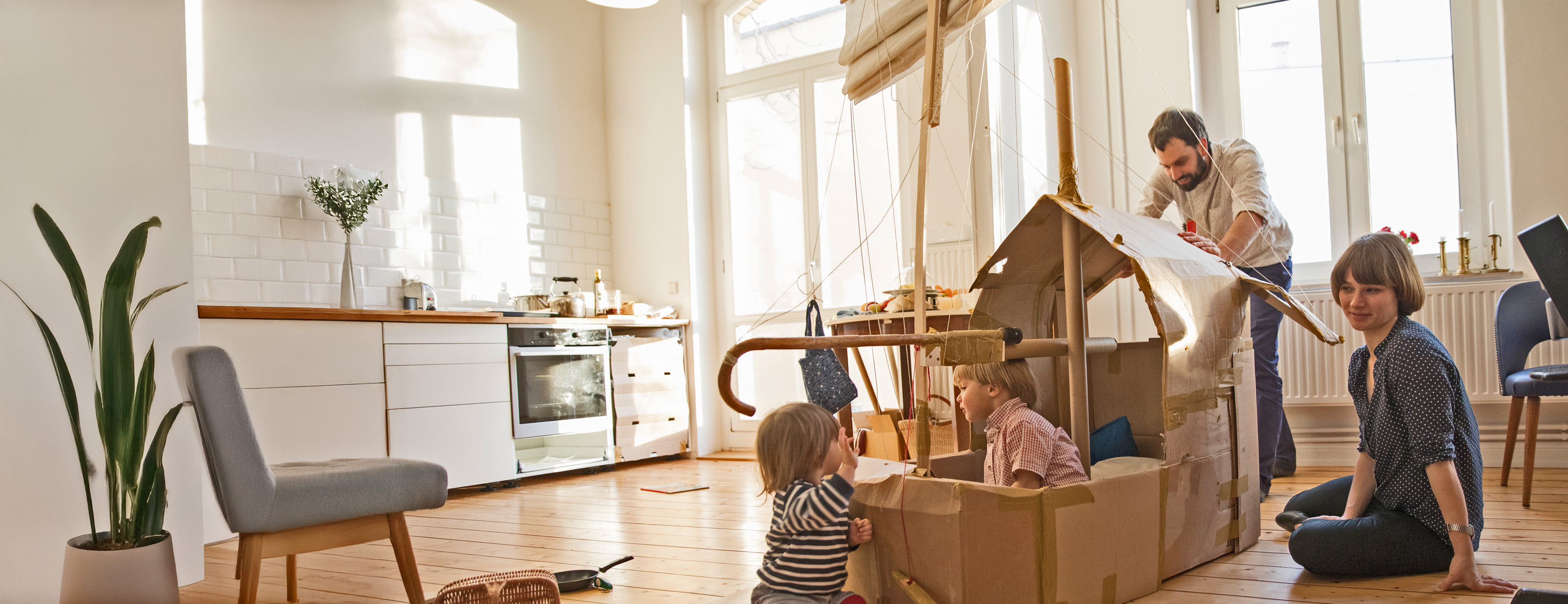 Kleine Kinder spielen mit den Eltern in einem Pappschiff in der Küche