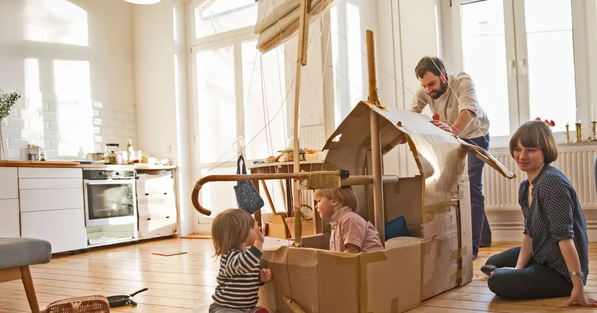 Kleine Kinder spielen mit den Eltern in einem Pappschiff in der Küche