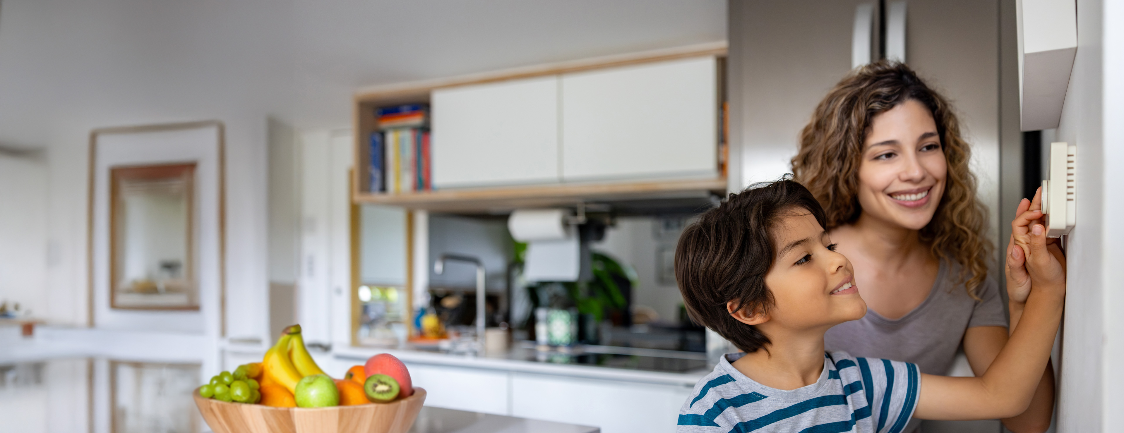 Mutter mit Sohn steht in der Küche und drehen am Thermostat